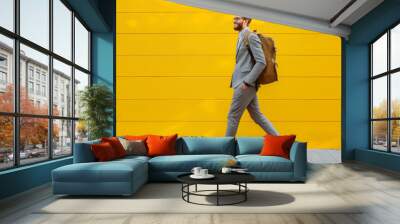 Smiling young businessman in costume with backpack walking outside near yellow wall, copy space Wall mural