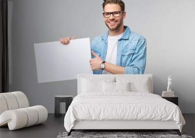 Portrait of a happy handsome young man holding blank white card or sign over white background Wall mural