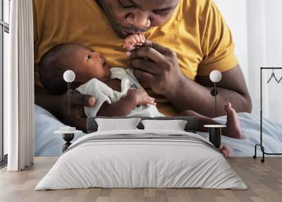 An African American father kissing hand,  his 12-day-old baby newborn son lying in bed in a white bedroom,with happy, concept to African American family and newborn Wall mural