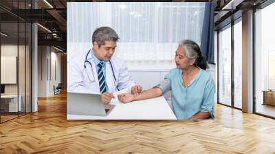 Asian man doctor is using a manual sphygmomanometer instrument for the woman elderly patient before analyze and treatment, to people health care and health insurance concept. Wall mural