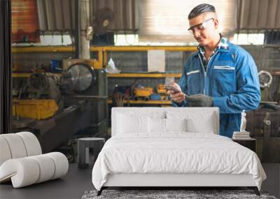 Engineers, experienced technicians Caucasian man are using mobile phone before working by controlling steel lathes, flange plates in parts production line at workplace in the industrial factory Wall mural