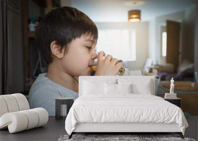 Healthy kid drinking fresh orange juice from clear glass and playing with his toy.New normal healthy lifestyle with child boy having breakfast with fesh food at home. Family time on dinning table Wall mural