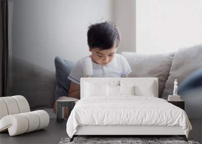 Kid eating coconut ice lolly while playing game on tablet,Hight key portrait Child sitting on sofa doing homework online at home,A boy playing games on internet with light shining from window Wall mural