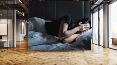 Depressed young man lying in the bed with hand covering his face  Wall mural