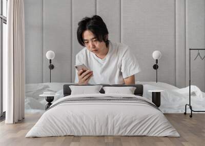 sleepy young man using smartphone on the bed  Wall mural