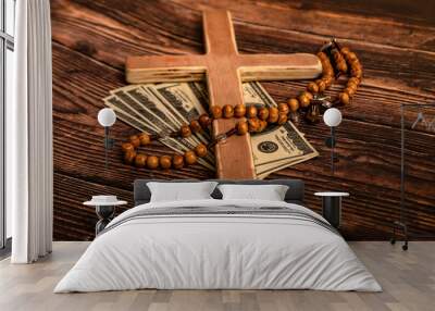 A Catholic cross, a rosary with beads and dollars lie on a dark brown wooden table. Wall mural