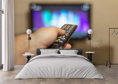 A person with a TV remote controls the remote control to switch channels to watch TV shows. Wall mural