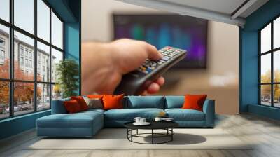 A person with a TV remote controls the remote control to switch channels to watch TV shows. Wall mural