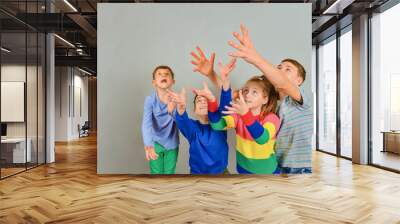 Emotional children pull their hands up in the hope of catching something, four children in colored clothes. Place for advertising and text. Wall mural