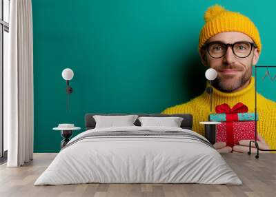 Portrait of a bearded man with a Christmas gift box wearing a yellow hat and eyeglasses.  Wall mural