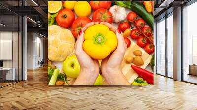 Close up of a cook holding a yellow pepper in her hands on a table with vegetables Wall mural