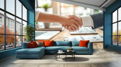 Two people shaking hands in front of a table with laptops and a clipboard Wall mural