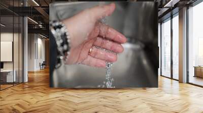 The hand of a man under the water of a kitchen tap. Man intent on washing his hands to disinfect bacteria and viruses. Wall mural