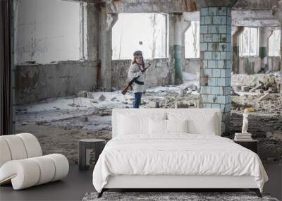 a little girl alone in an abandoned and ruined building with a Kalashnikov assault rifle and arms making her way to survive Wall mural