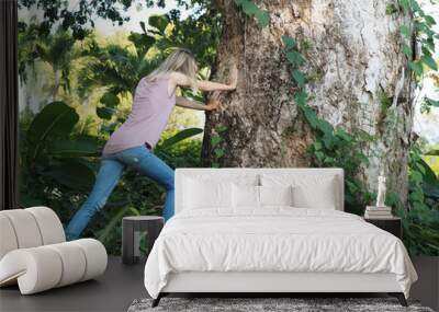 An attractive woman pushes a large tree in nature in the summer. Wall mural