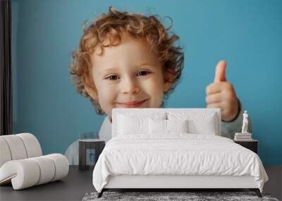 Curly boy with thumb up. A child from elementary school in uniform. Baby indoors on a blue background Wall mural