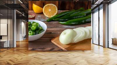 Green hot chili pepper and cut onion on cutting board with lemon on wooden background Wall mural