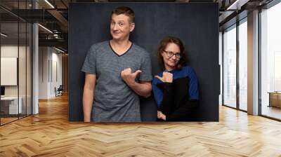 Shot of man and woman pointing with thumbs at one another Wall mural