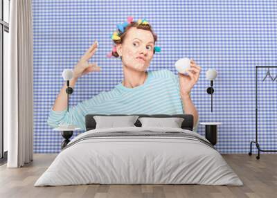 Woman with skincare product on face, with bright hair curlers on head Wall mural