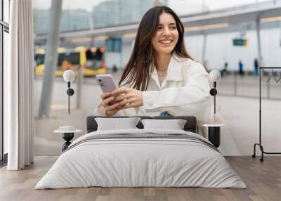 Waiting for the bus and for love. Bright cheerful young woman of Turkish mixed race in white casual clothes with a charming smile holding a phone in the street at public transportation stop Wall mural