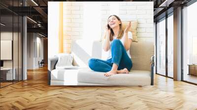 young woman at home on sofa cheerfully speaking on phone or gossiping with her friend Wall mural