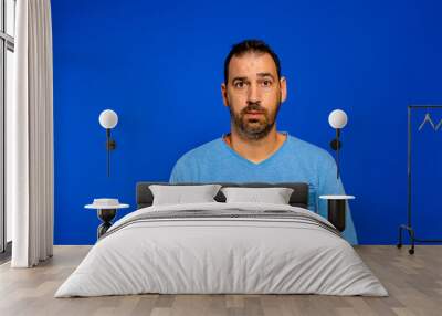 Bearded man in pajamas who just woke up and had a nightmare, he is serious and sad that he has relived a past trauma. Isolated on blue studio background Wall mural