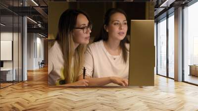 Selective focus shot of two young ladies looking at the computer screen and taking notes Wall mural