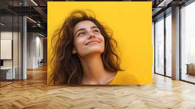 Beautiful young woman smiling and looking up on yellow background Wall mural