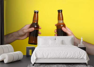 Two male hands holding up beer bottles making a toast on yellow background Wall mural