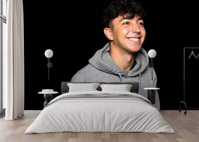 Portrait of young Caucasian man with curly hair about 25 years old, smiling while posing on black background Wall mural