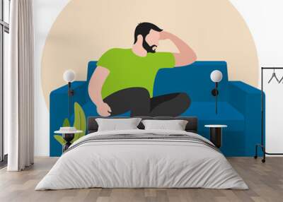 Handsome Pensive Man Sitting On Sofa In Apartment. He sits with his foot on his leg and leans on his elbow. Flat design. Vector illustration on white background Wall mural