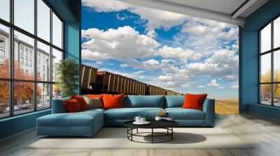 cargo train disappears into the distance under a cloudy sky Wall mural