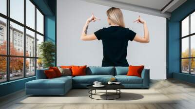 Back of stylish blonde girl wearing black t-shirt posing in studio Wall mural