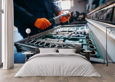 Blurred background of male hands of auto mechanic in yellow work gloves holding wrenches above a set of tools from wrenches and heads for unscrewing nuts and bolts in a special cabinet Wall mural