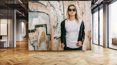 Girl wearing t-shirt, glasses and leather jacket posing against street , urban clothing style. Street photography Wall mural