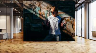 Girl wearing t-shirt, glasses and leather jacket posing against street , urban clothing style. Street photography Wall mural