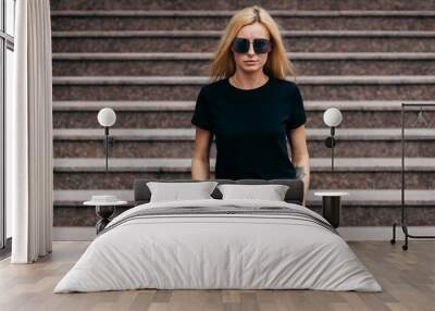 Stylish blonde girl wearing black t-shirt and glasses posing against street , urban clothing style. Street photography Wall mural