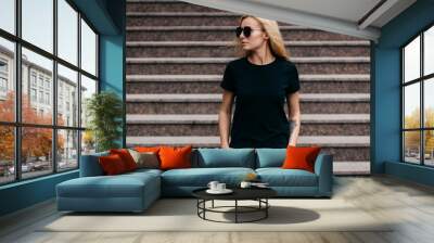 Stylish blonde girl wearing black t-shirt and glasses posing against street , urban clothing style. Street photography Wall mural