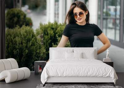 Stylish brunette girl wearing black t-shirt and glasses posing against street , urban clothing style. Mock up Wall mural