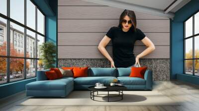 Stylish brunette girl wearing black t-shirt and glasses posing against street , urban clothing style. Street photography Wall mural