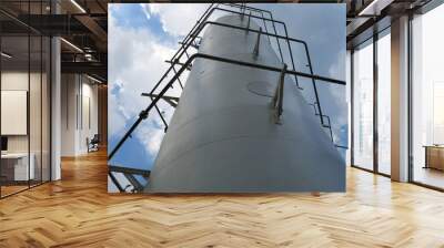 Close-up view from below to the top of buffer tank in LNG facility on cloudy day Wall mural