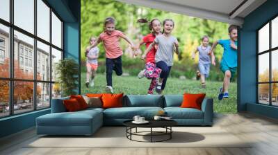 A group of happy children of boys and girls run in the Park on the grass on a Sunny summer day . The concept of ethnic friendship, peace, kindness, childhood. Wall mural