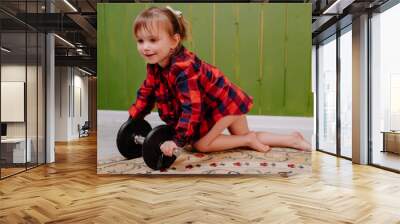 A little girl in a red shirt plays with daddy's dumbbells.  Wall mural