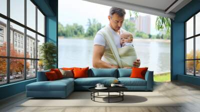 Father carrying his son in sling outdoors Wall mural