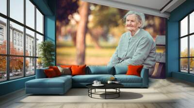 Portrait of senior woman sitting on bench in autumn park. Old lady feeling lonely and sad. Wall mural