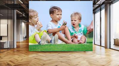 Two older boys eating ice cream, young woman wiping hands of youngest son Wall mural