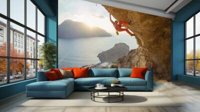 Young man climbing challenging route in cave at sunset, his partner belaying Wall mural