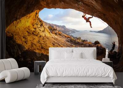 Young woman lead climbing in cave, male climber belaying Wall mural