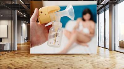 breast pump against background of blurred mother nursing baby with breast milk. Wall mural