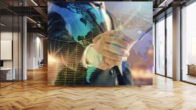 Double exposure of world map on cityscape background with two businessmen handshake. Concept of international business Wall mural